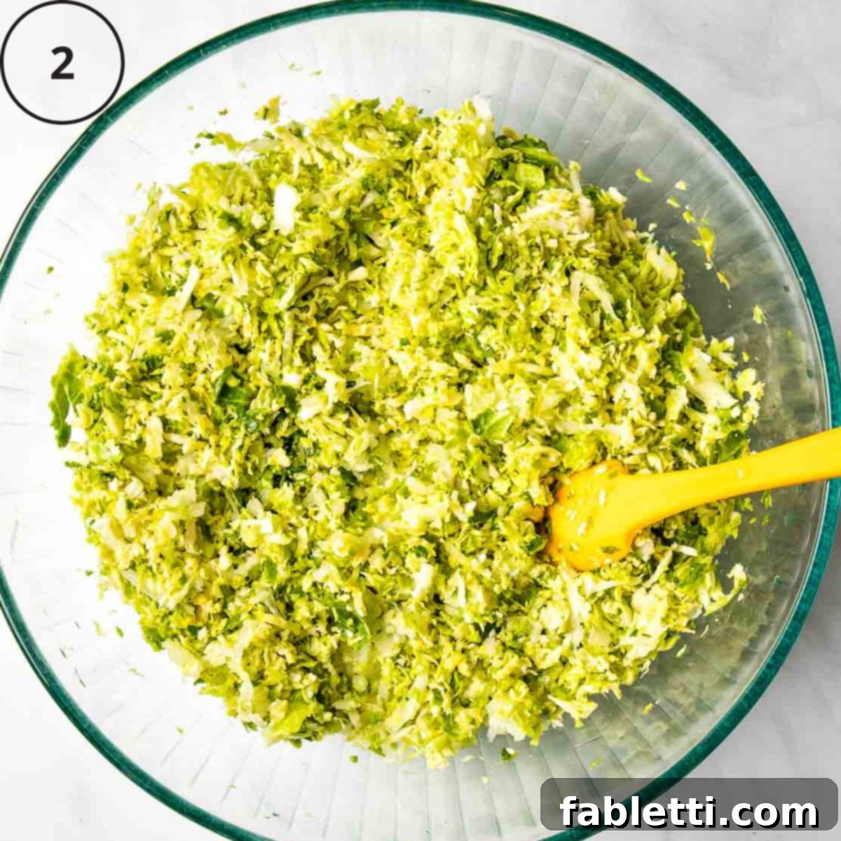 Oven-Baked Crispy Brussels Sprout Latkes 5 A large glass bowl brimming with a vibrant mix of freshly shredded Brussels sprouts and onions, ready for the next steps.