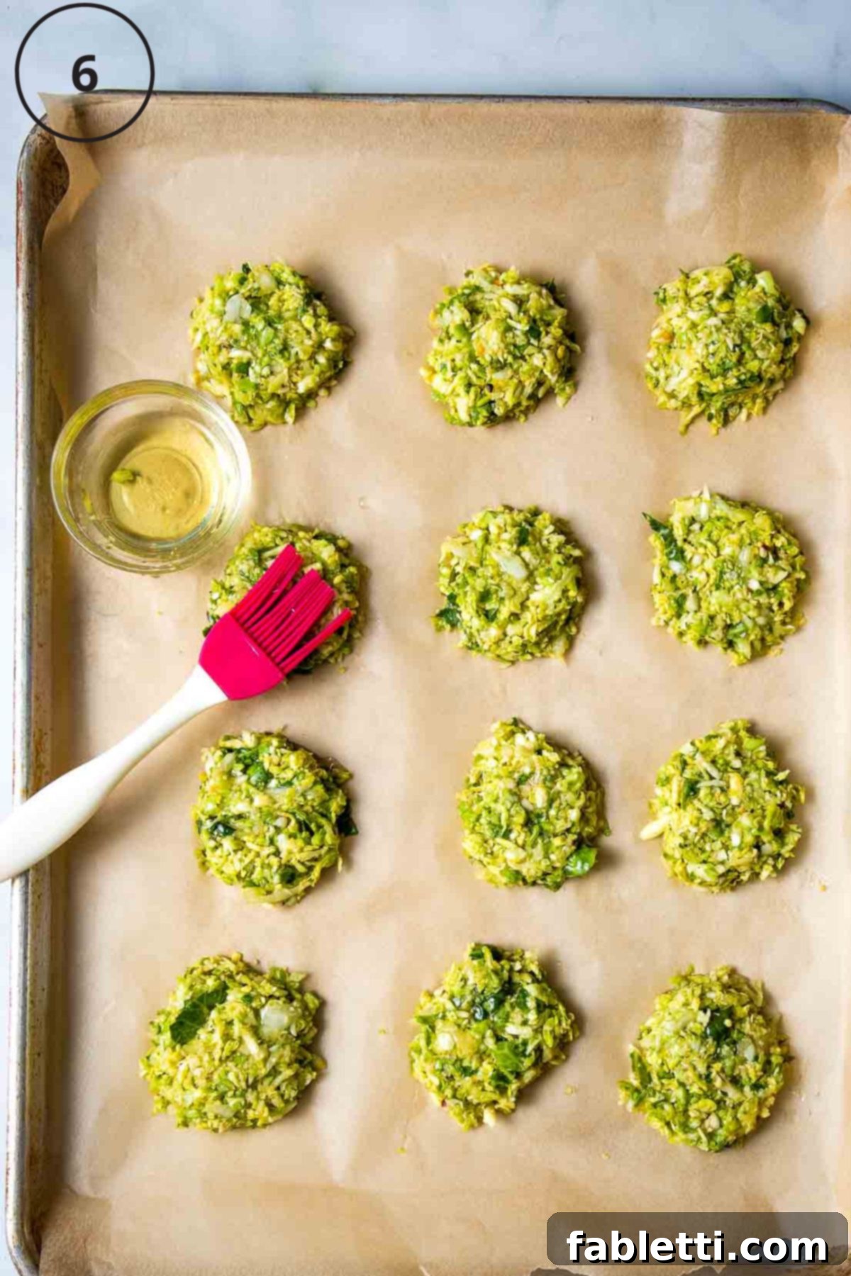 Oven-Baked Crispy Brussels Sprout Latkes 9 A pastry brush applies a thin layer of avocado oil onto Brussels sprouts latkes arranged on a parchment-lined baking sheet, preparing them for baking.