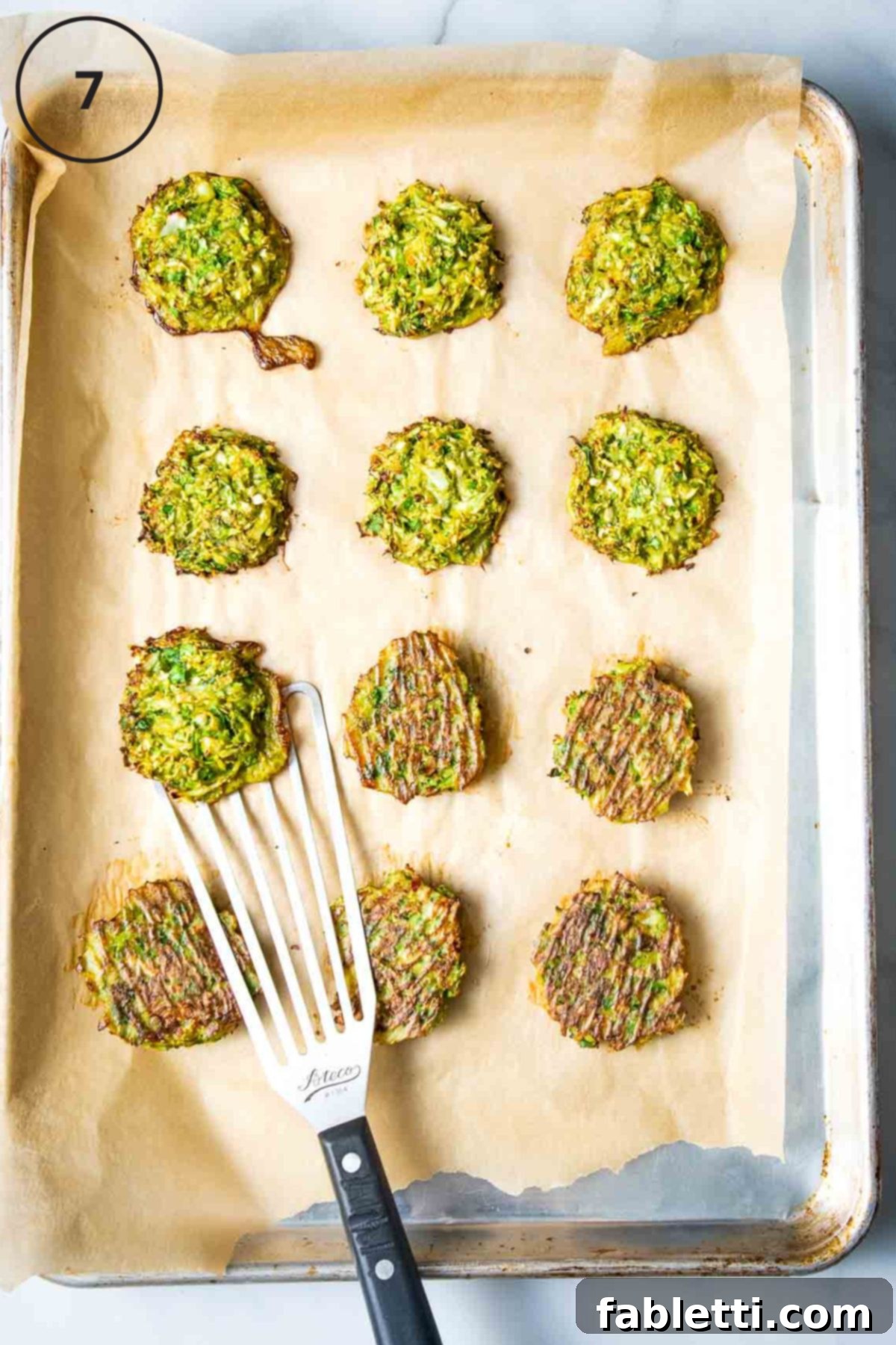 Oven-Baked Crispy Brussels Sprout Latkes 10 A spatula gently flips crispy Brussels sprouts latkes on a parchment-lined baking tray, ensuring even golden-brown cooking.