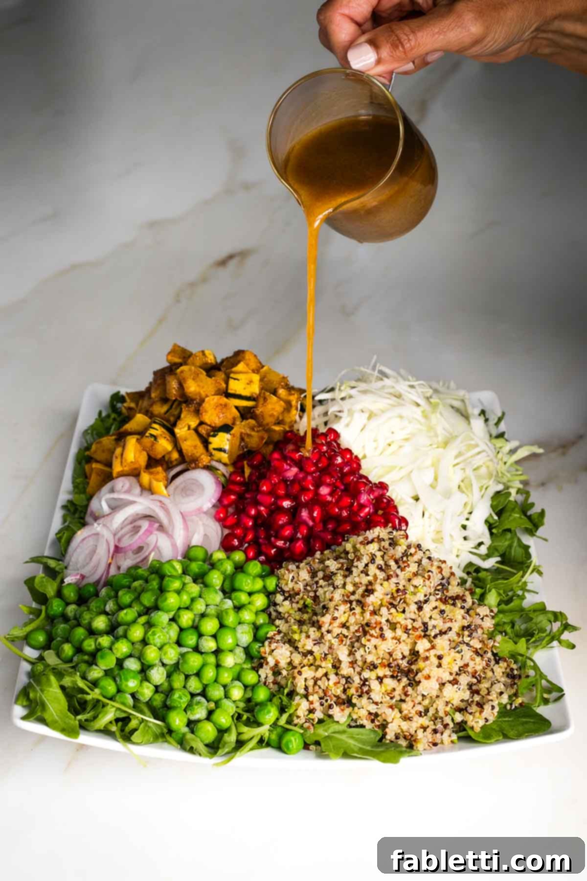 Pouring dressing onto cooked and raw, colorful veggies on a platter of arugula. 
