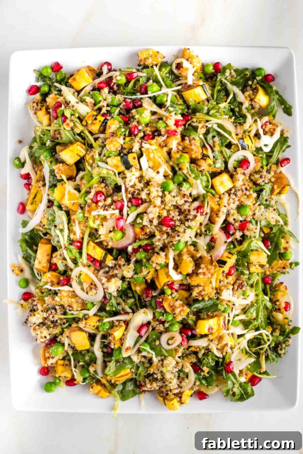 Platter of tossed arugula and quinoa salad with pomegranate, peas and roasted cubes of squash.