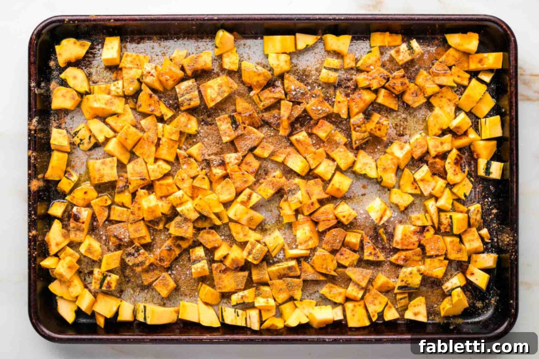 Rimmed baking tray with cubes of squash that have been sprinkled with warm spices.