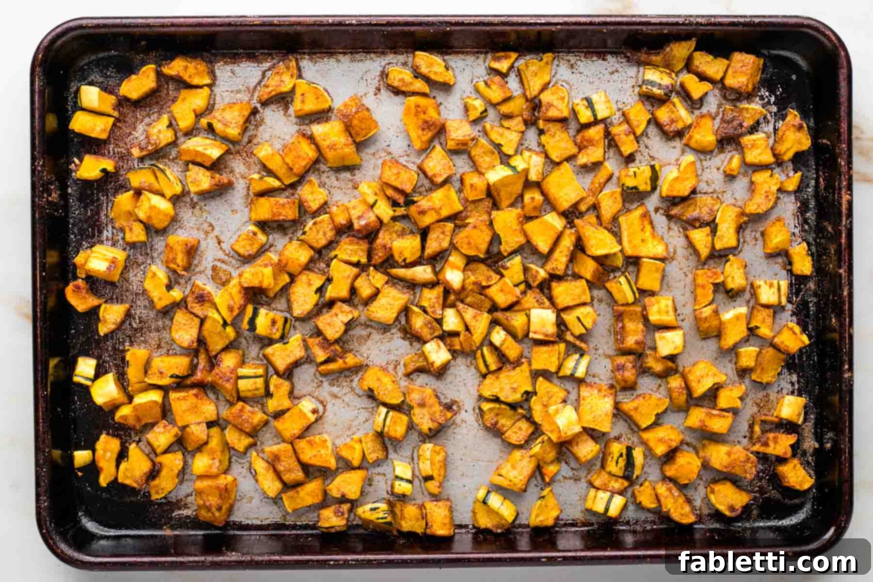 Seasoned and roasted cubes of squash on a rimmed baking sheet. 