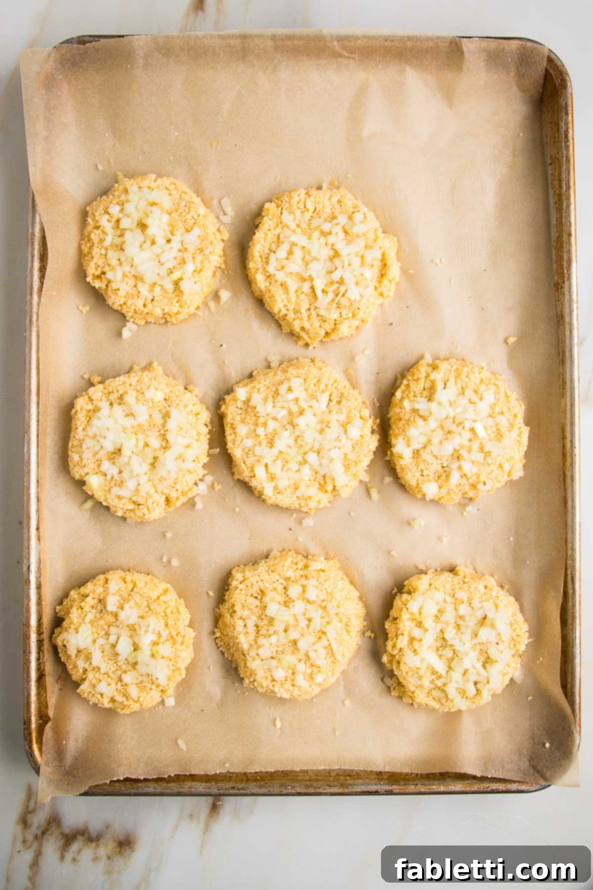 Flavorful Cauliflower Onion Buns 8 A parchment-lined baking tray showcasing eight perfectly formed cauliflower onion rolls, topped with extra onions, poised for baking.