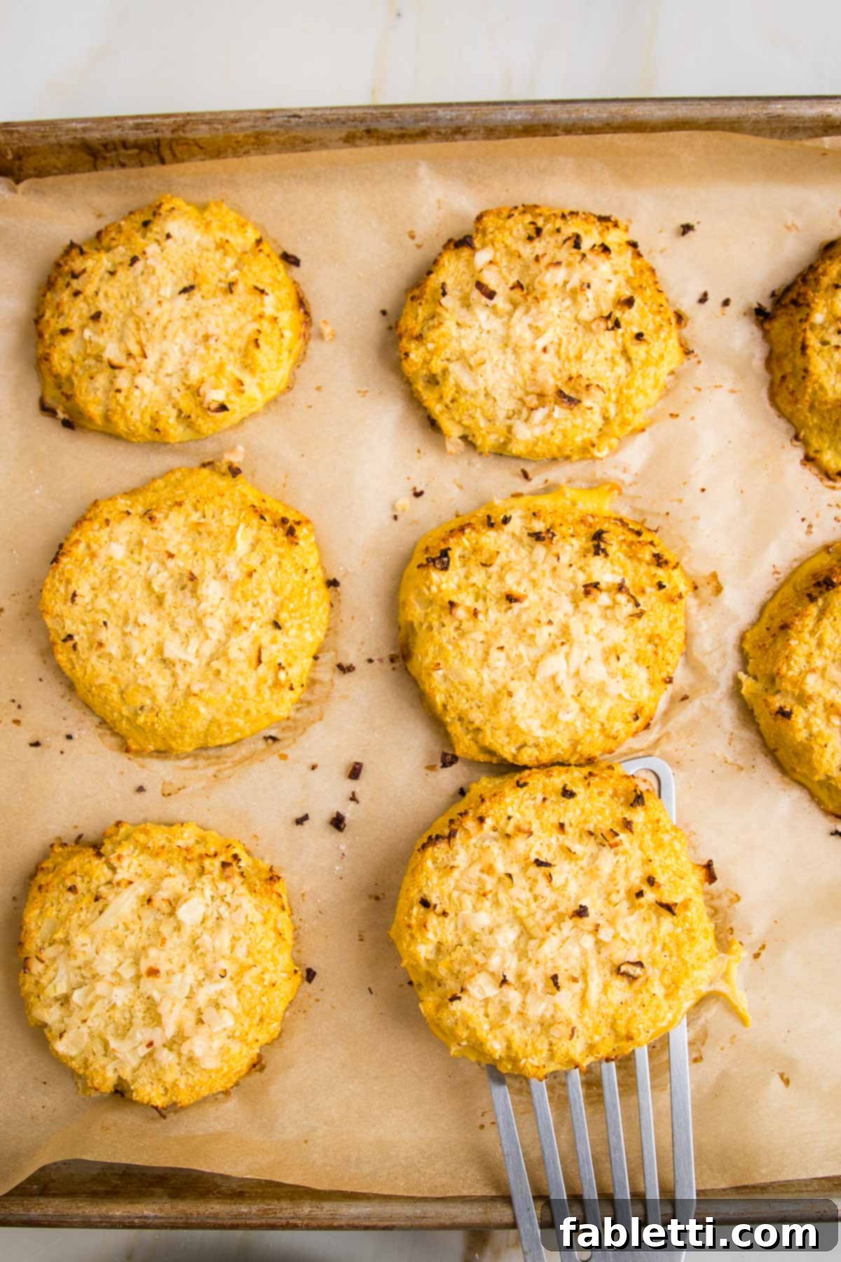Flavorful Cauliflower Onion Buns 9 A spatula gently lifting a golden-brown cauliflower onion roll from a baking tray, highlighting its perfect texture and readiness to serve.
