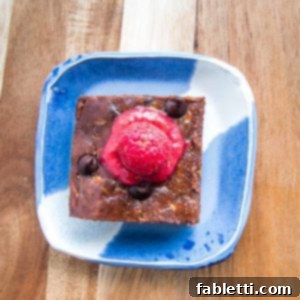 Secret Garden Chocolate Brownies 8 brownie on a bright blue plate with raspberry sauce on top.