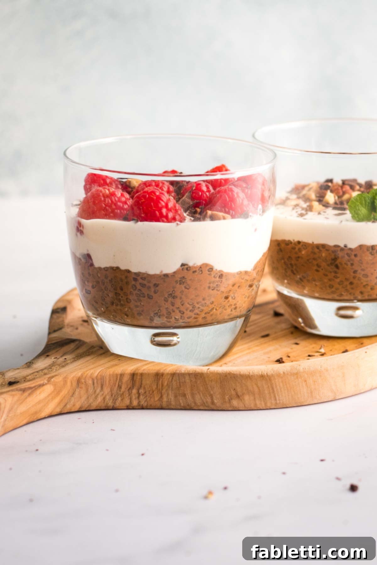 Effortless Chocolate Chia Pudding Bliss 3 Chocolate chia pudding in a glass, topped with cashew cream and fresh raspberries.