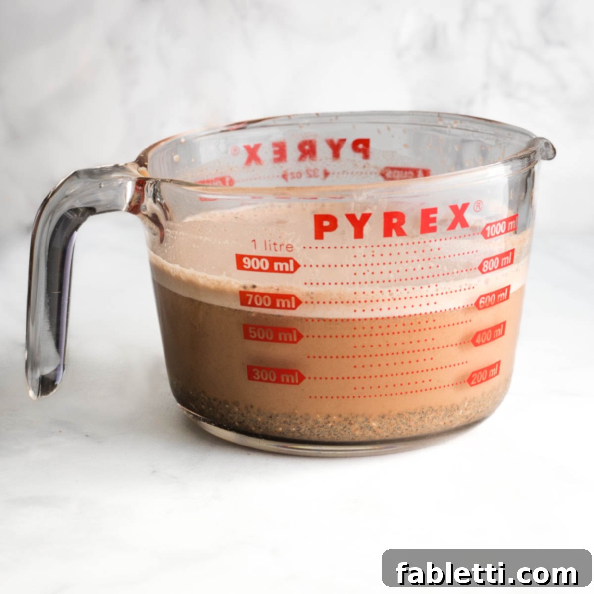 Effortless Chocolate Chia Pudding Bliss 10 Glass measuring cup with chocolate milk at the top and chia seeds that sunk to the bottom.