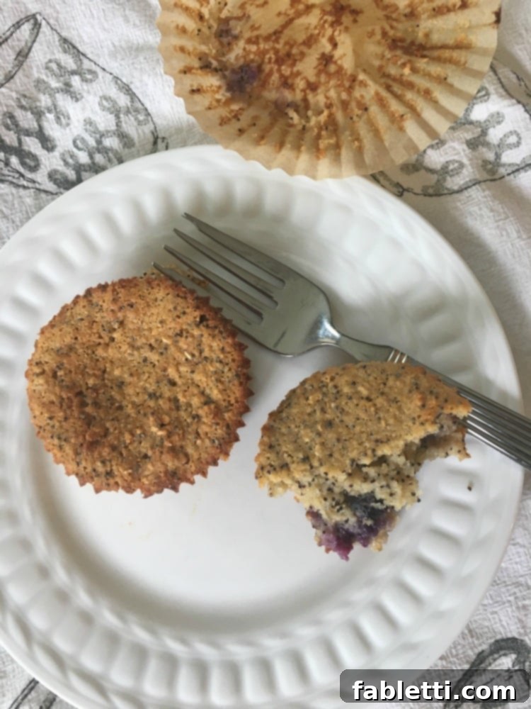 Bright Gluten-Free Blueberry Lemon Poppy Seed Muffins 2 White plate showcasing a blueberry lemon poppyseed muffin cut open, revealing its moist, tender interior.