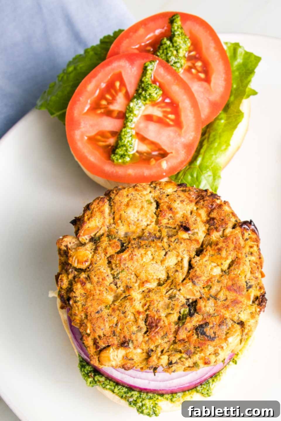 Hearty Homemade White Bean Veggie Burgers 11 A beautifully assembled white bean burger on a toasted bun, garnished with vibrant tomatoes, crisp lettuce, red onions, and a luscious drizzle of green arugula aioli.