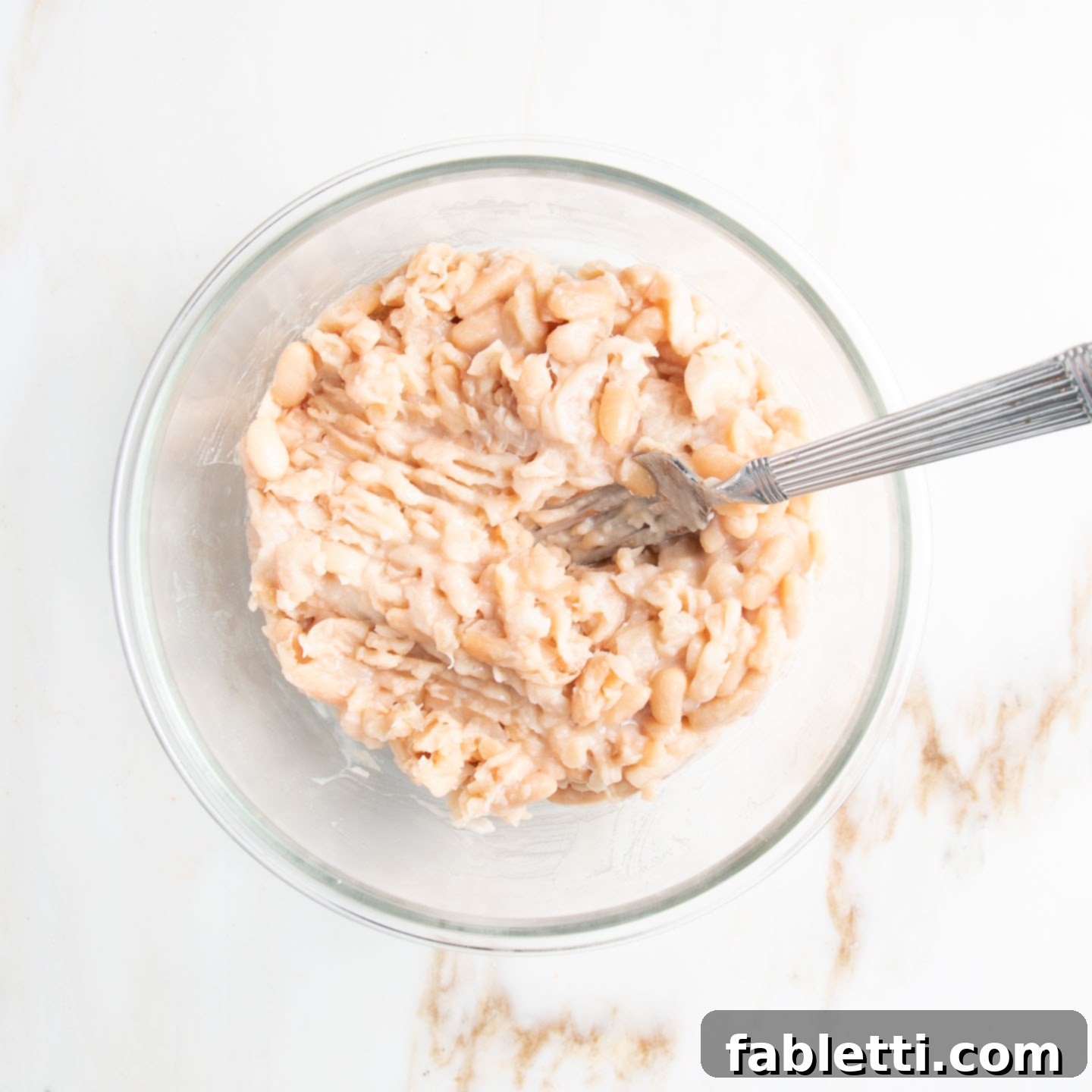 Hearty Homemade White Bean Veggie Burgers 5 A bowl containing mashed white beans, with a fork resting inside, ready for the next step of mixing.