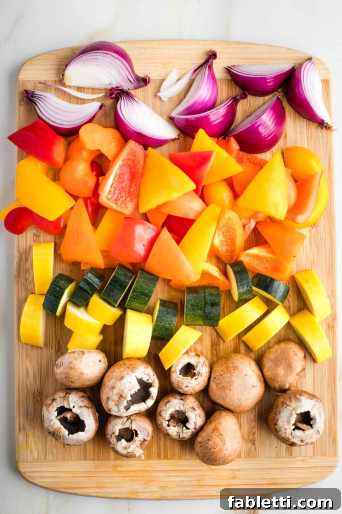 Vibrant Mediterranean Veggie Skewers 4 Cutting board displaying large, uniformly cut chunks of red onion, bell peppers, zucchini, yellow squash, and baby bella mushrooms, ready for skewering.
