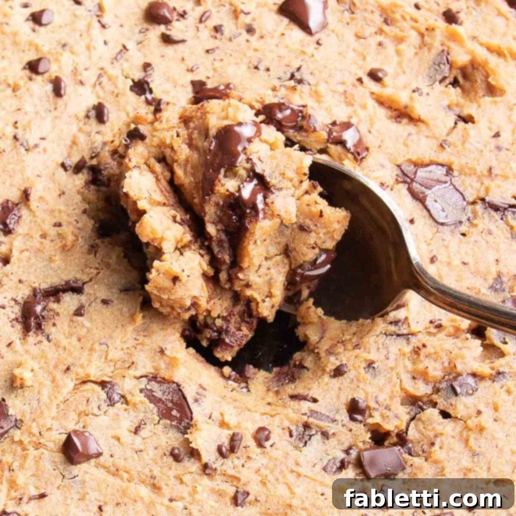 Decadent Vegan Gluten-Free Chocolate Chunk Skillet Cookie 11 A close-up shot of a spoon sinking into the warm, gooey, undercooked center of a chocolate chunk skillet cookie.
