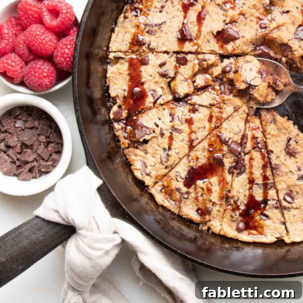 Decadent Vegan Gluten-Free Chocolate Chunk Skillet Cookie 12 A gorgeous chocolate chunk skillet cookie artfully drizzled with date syrup, surrounded by extra chocolate pieces and fresh, vibrant raspberries.