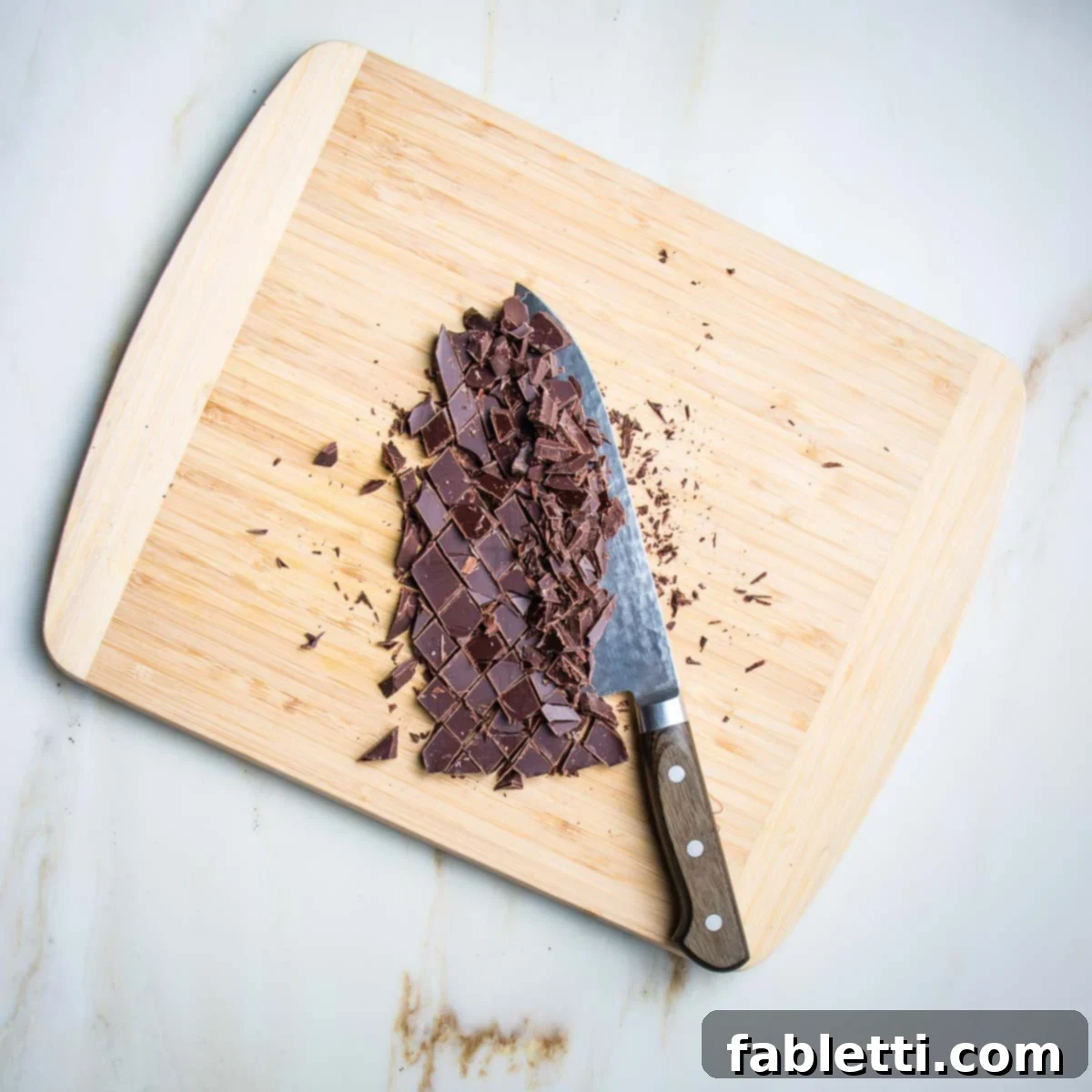 Decadent Vegan Gluten-Free Chocolate Chunk Skillet Cookie 7 A dark chocolate bar expertly chopped into rustic chunks on a rustic wooden cutting board.
