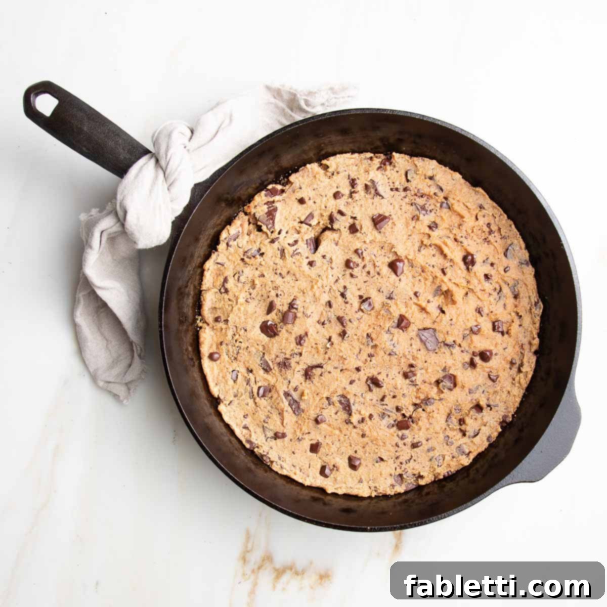 Decadent Vegan Gluten-Free Chocolate Chunk Skillet Cookie 10 A freshly baked, golden-brown chocolate chunk cookie sits in a cast iron skillet, edges perfectly set and center beautifully soft.
