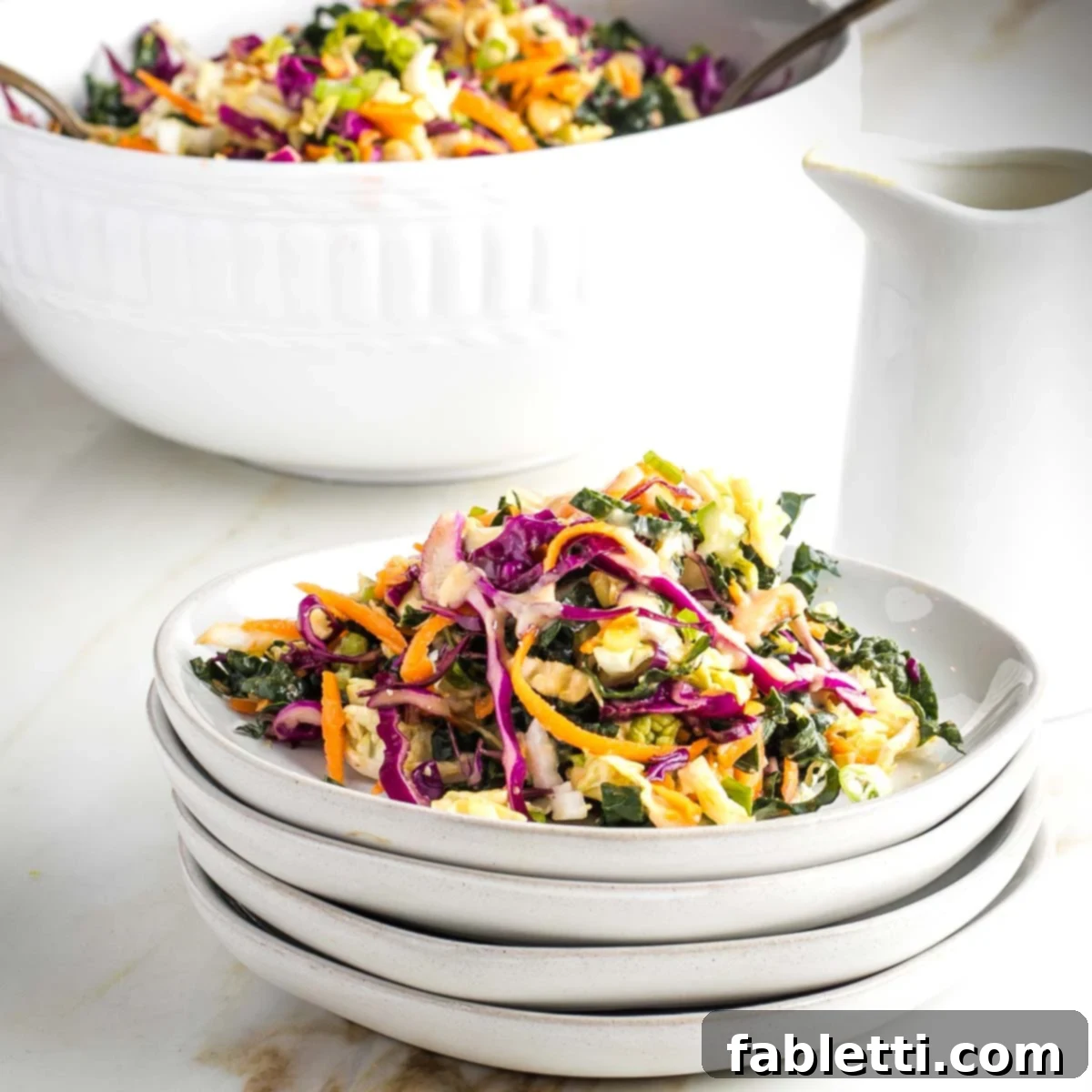 A beautifully arranged serving of colorful Summer Slaw with Ginger Miso Dressing on a plate, with a larger serving bowl in the background.