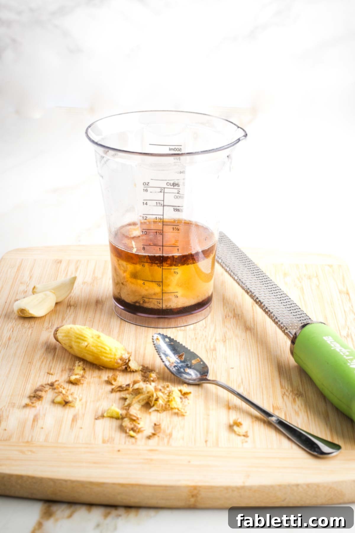 A peeled knob of fresh ginger sits next to a jar containing liquid ingredients for the dressing, ready for blending.