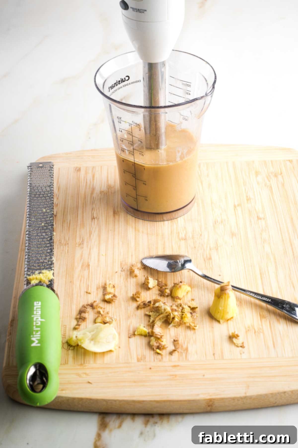 An immersion blender actively mixing the light brown, creamy dressing in a tall container.