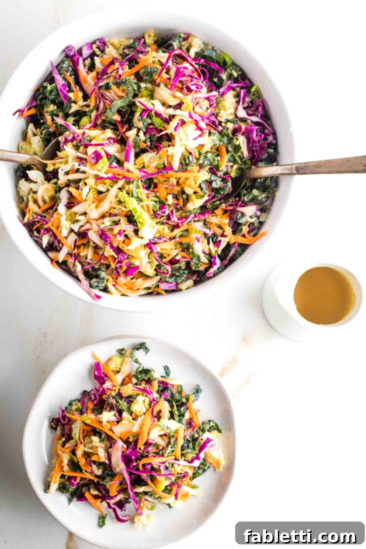 A beautifully presented bowl of bright, colorful coleslaw, with a small individual plate of slaw and a pitcher of extra dressing alongside.