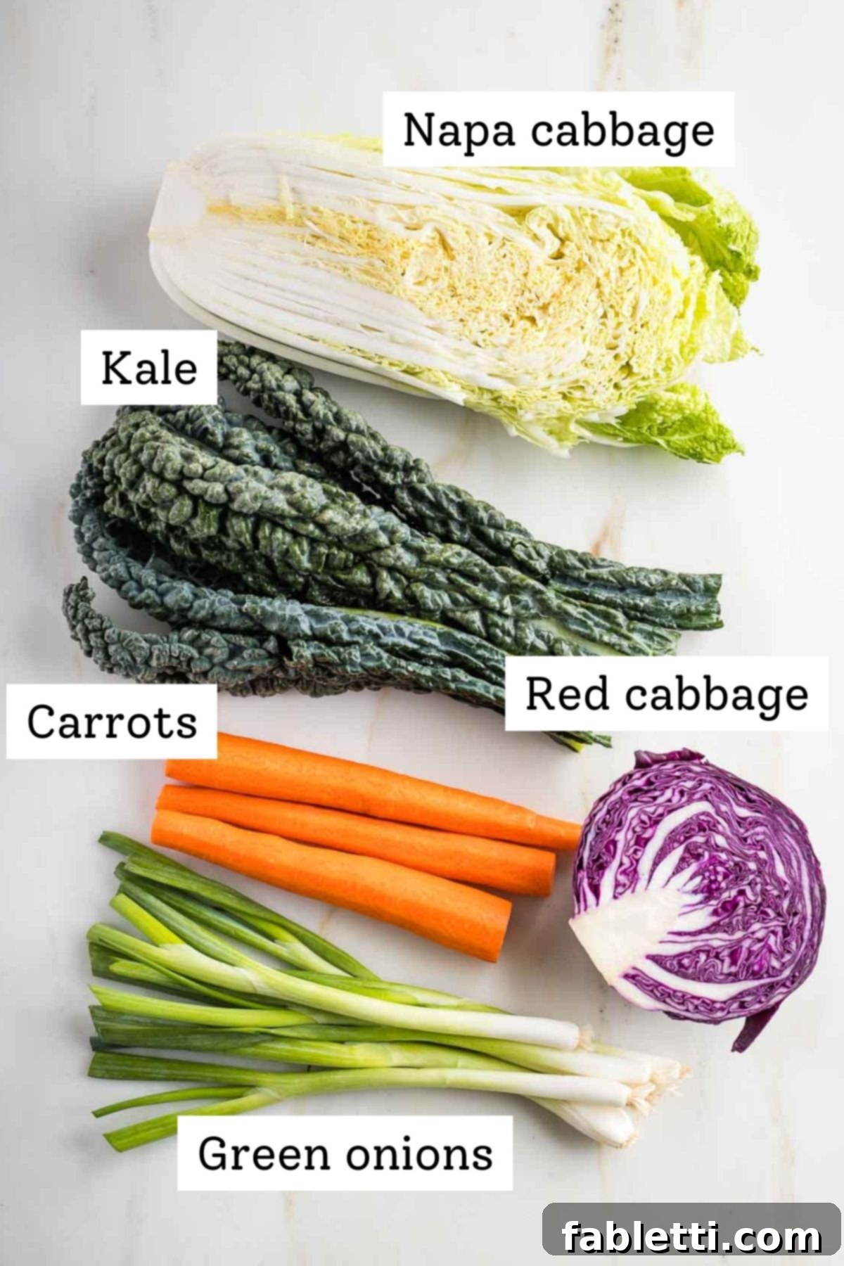 A display of fresh, whole ingredients for the slaw: vibrant Napa cabbage, curly kale, bright carrots, crisp green onions, and deep red cabbage.