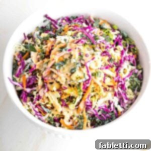 A large bowl brimming with colorful cabbage, carrots, and kale, generously coated in a creamy dressing.