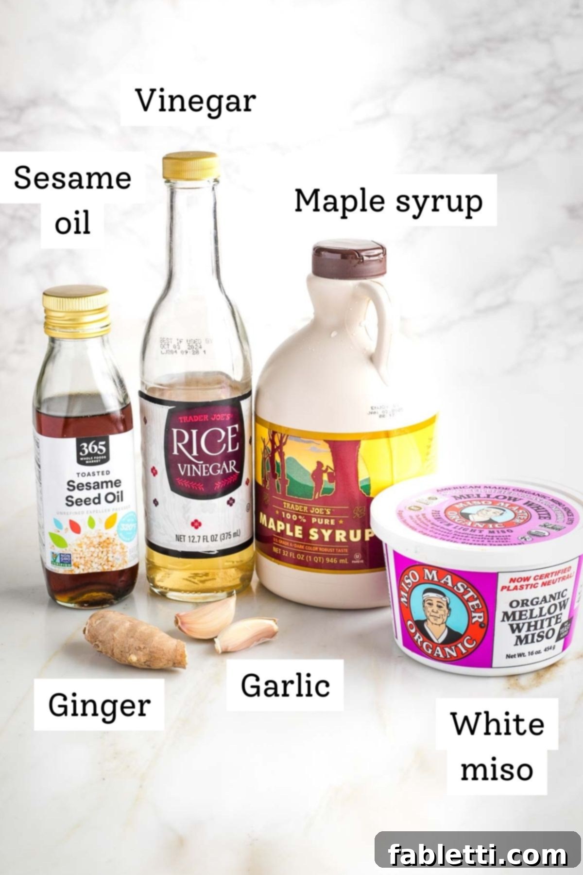 Close-up of the essential ingredients for Ginger Miso Dressing: miso paste, sesame oil, rice vinegar, maple syrup, fresh ginger, and garlic.