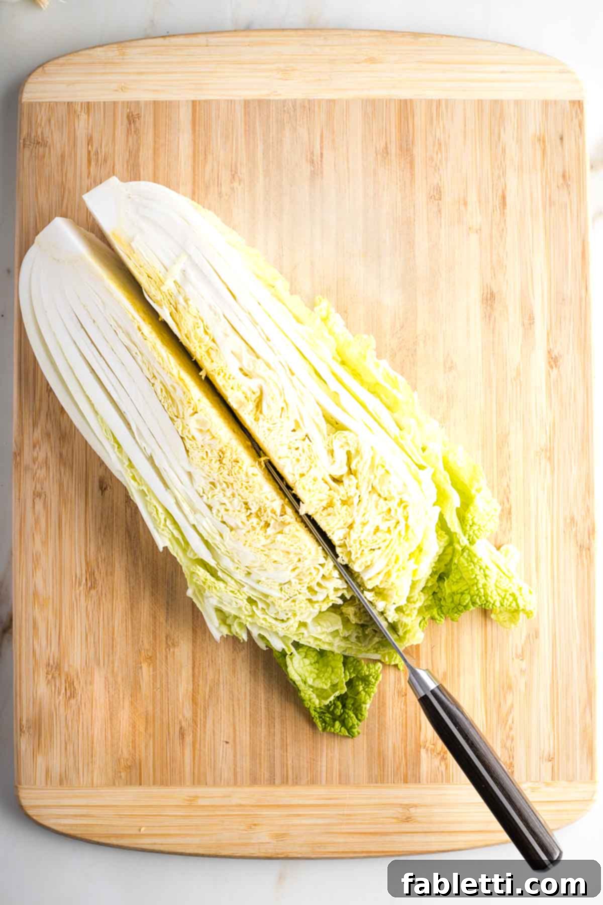 A Napa cabbage being cut lengthwise through its core.