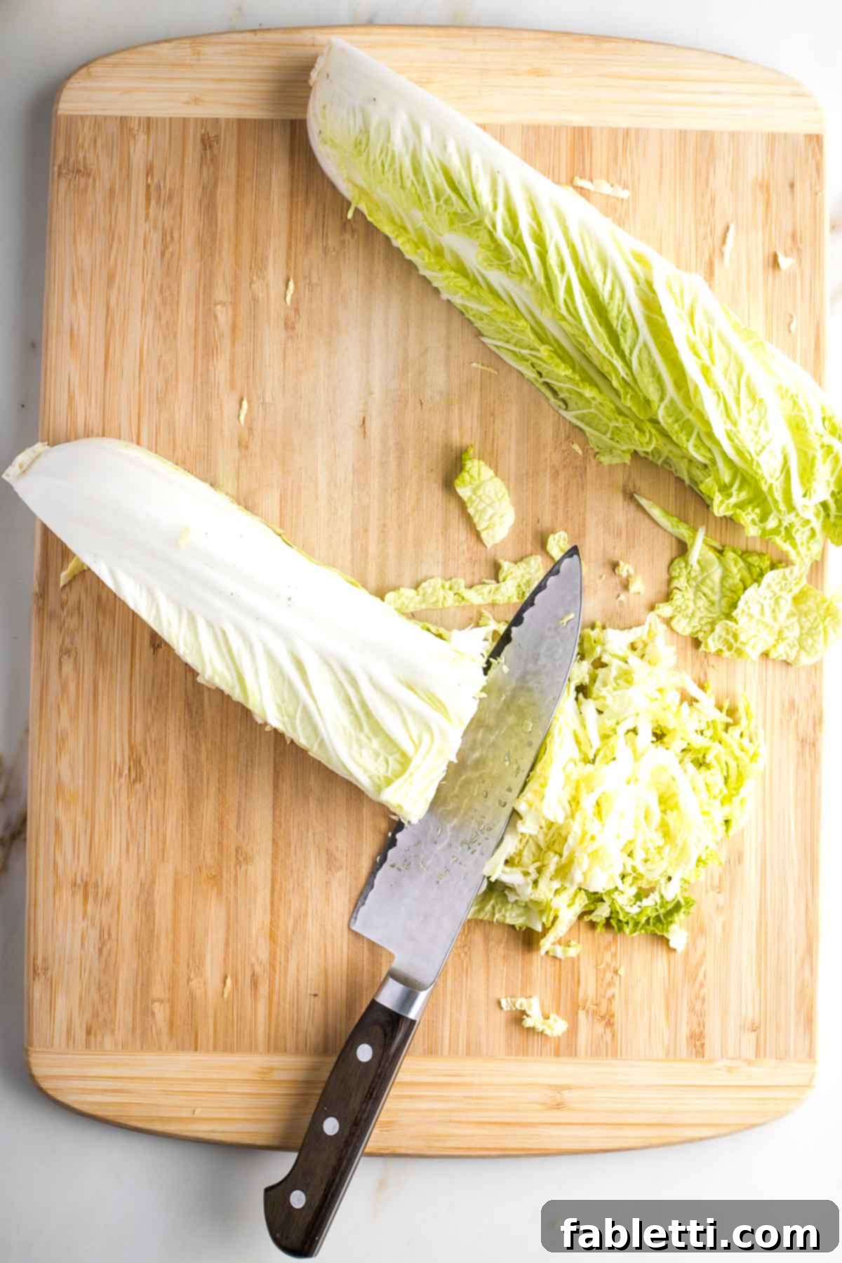 Quartered Napa cabbage being thinly sliced across into ribbons.