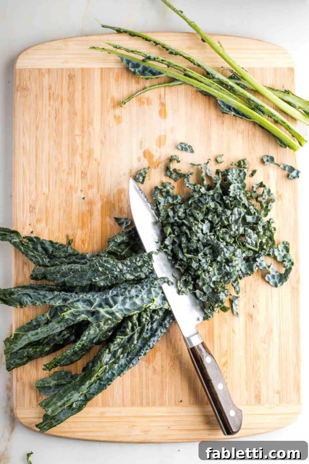 De-stemmed lacinato kale leaves being thinly sliced into strips.