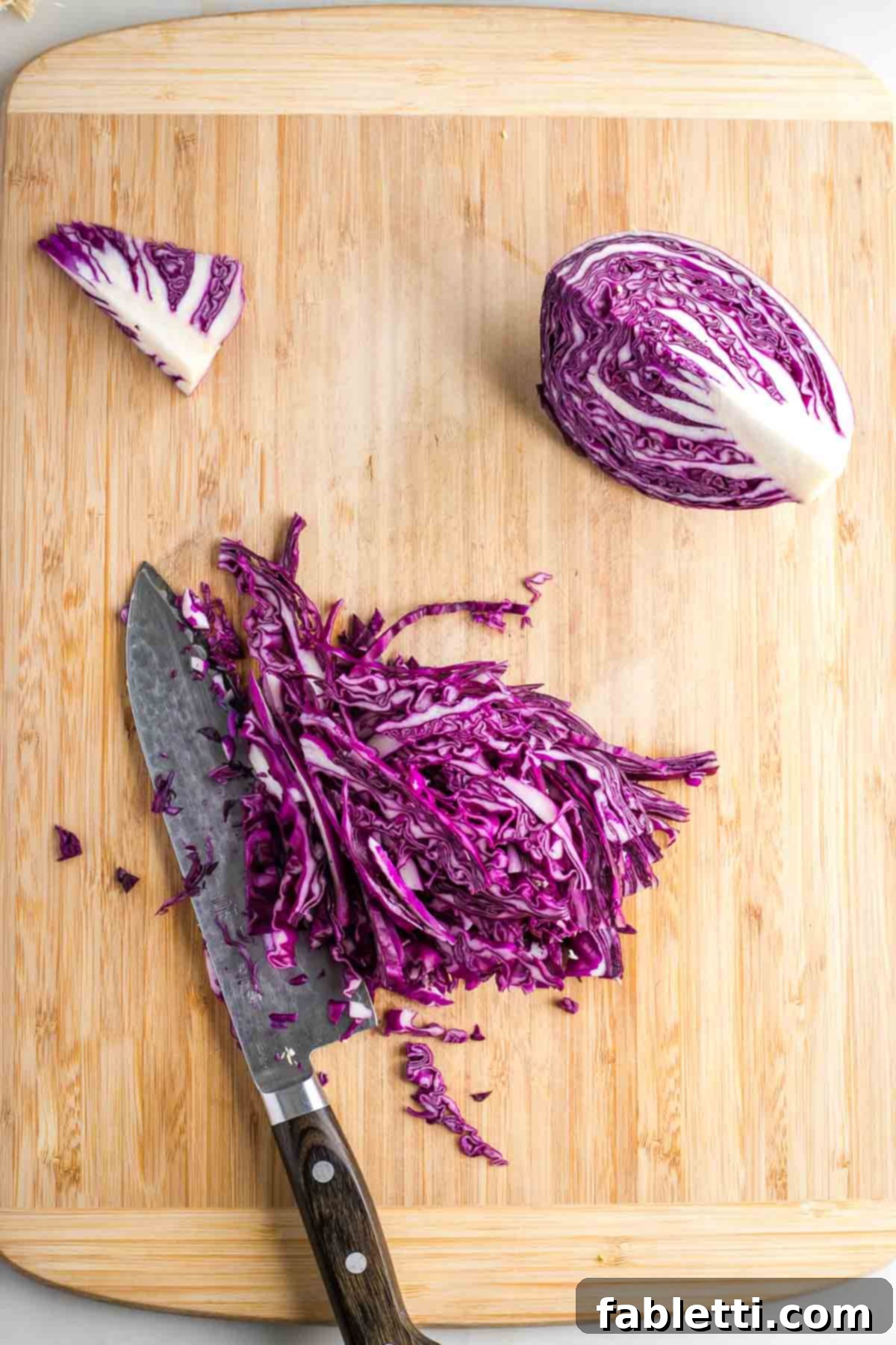 A quartered red cabbage with the woody core removed, with one quarter thinly sliced.