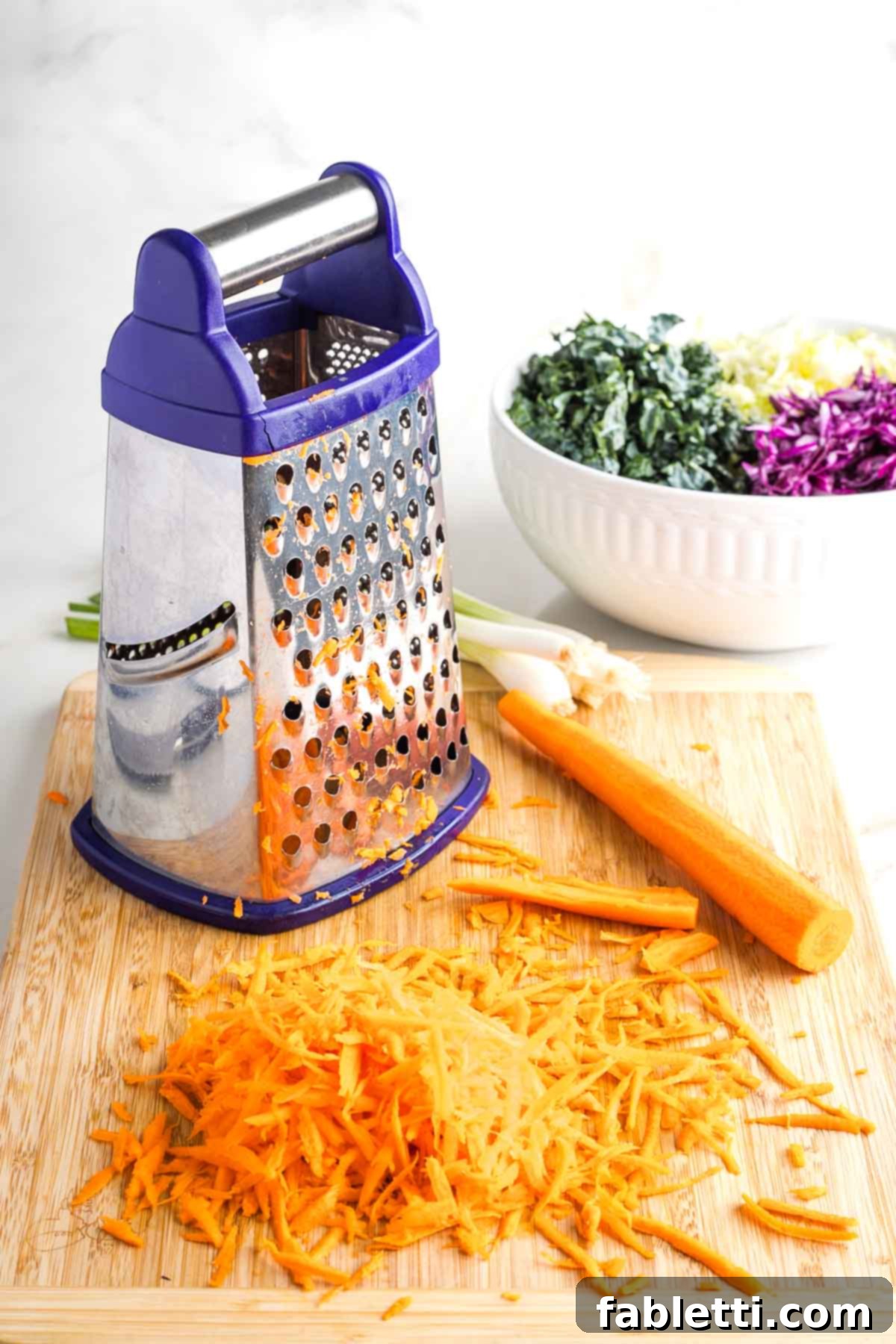 Shredding carrots using a box grater, with a bowl of prepared cabbage in the background.