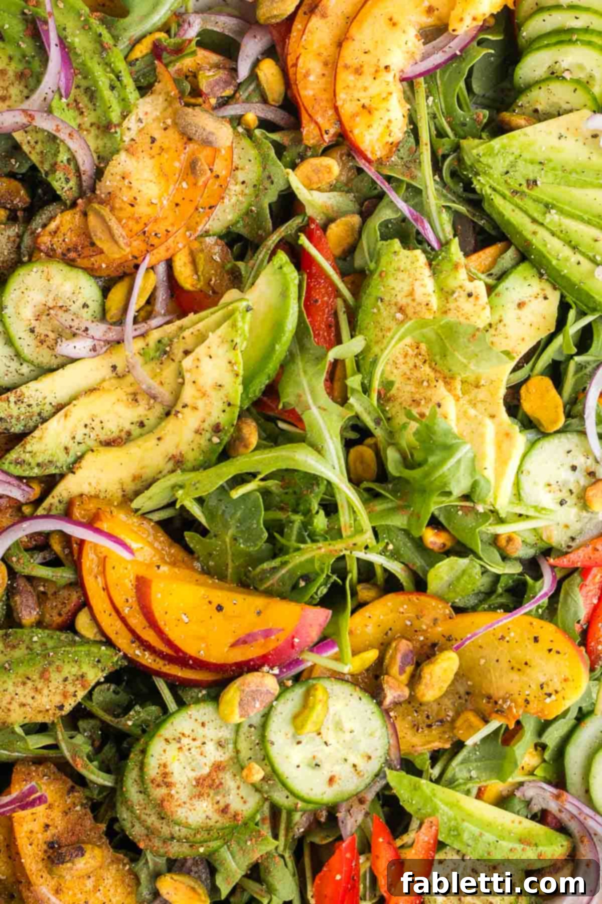 Vibrant Nectarine Arugula Salad 3 Close-up of fresh nectarine, avocado, cucumber, and red pepper slices, seasoned with cinnamon, salt, pepper, and sprinkled with pistachios.