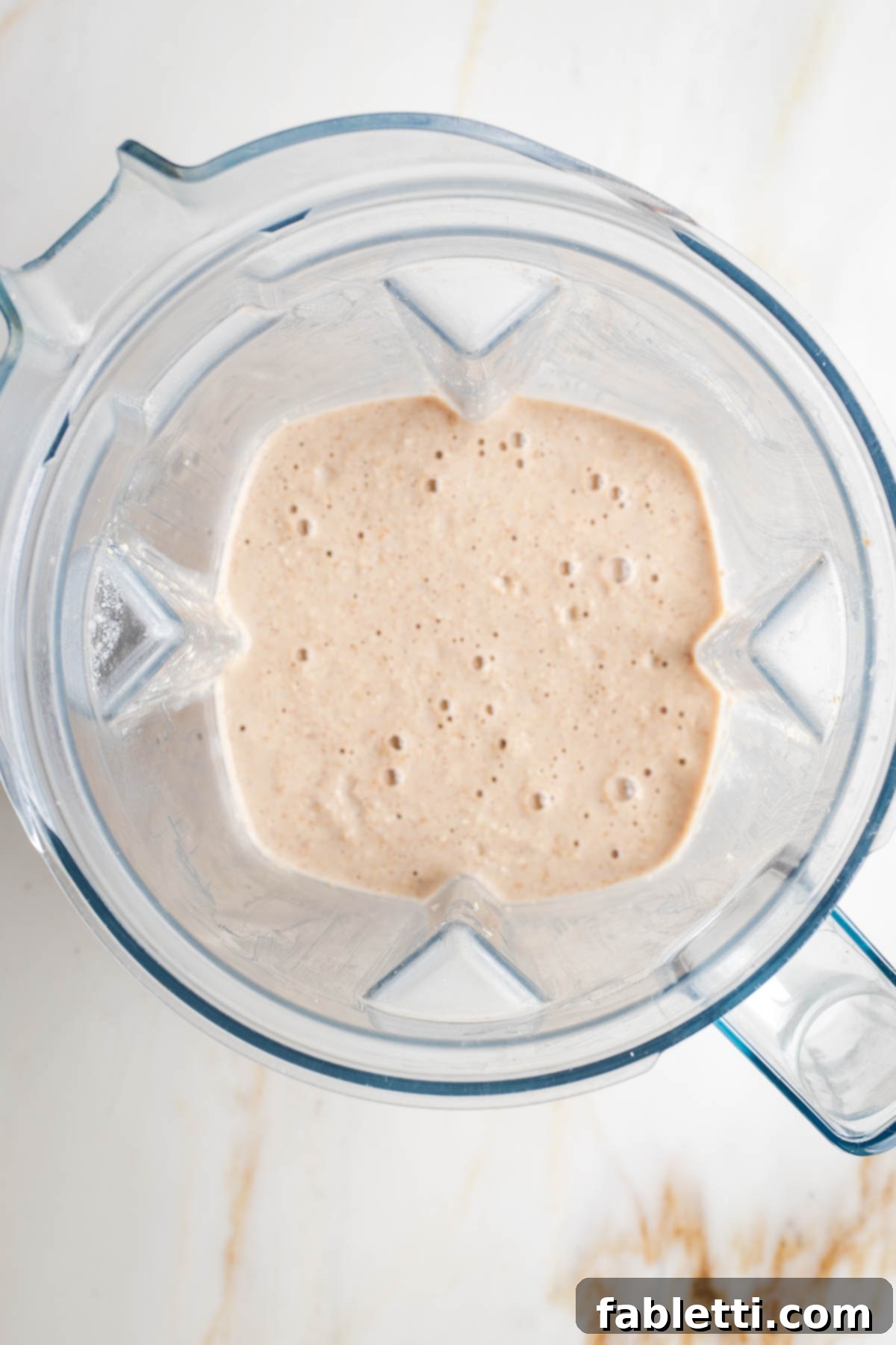 Effortless Vegan Banana Oat Blender Pancakes 5 Top view of a blender pitcher with a beige batter with air bubbles.