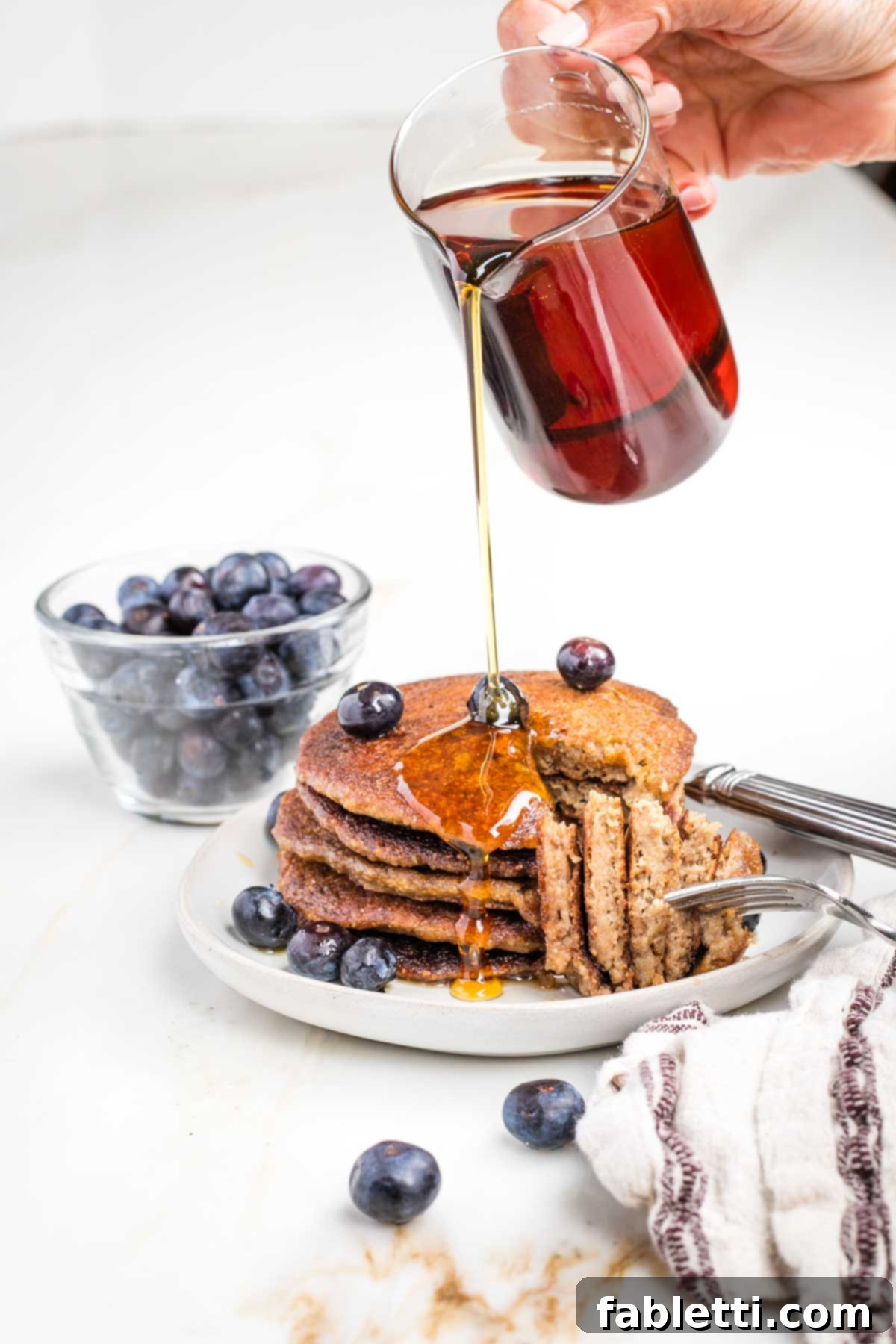 Effortless Vegan Banana Oat Blender Pancakes 8 A bite cut out of a stack of banana oatmeal pancakes with maple syrup being poured over the plate.