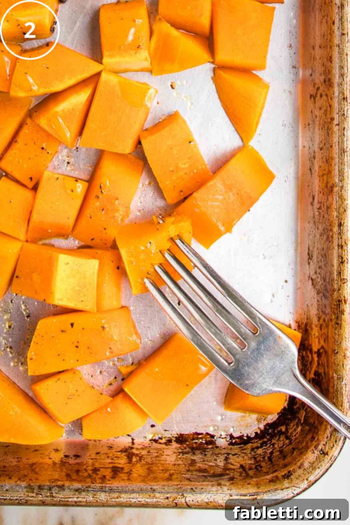 Velvety Vegan Butternut Bliss 11 A fork piercing a cube of roasted squash on a large rimmed baking sheet.