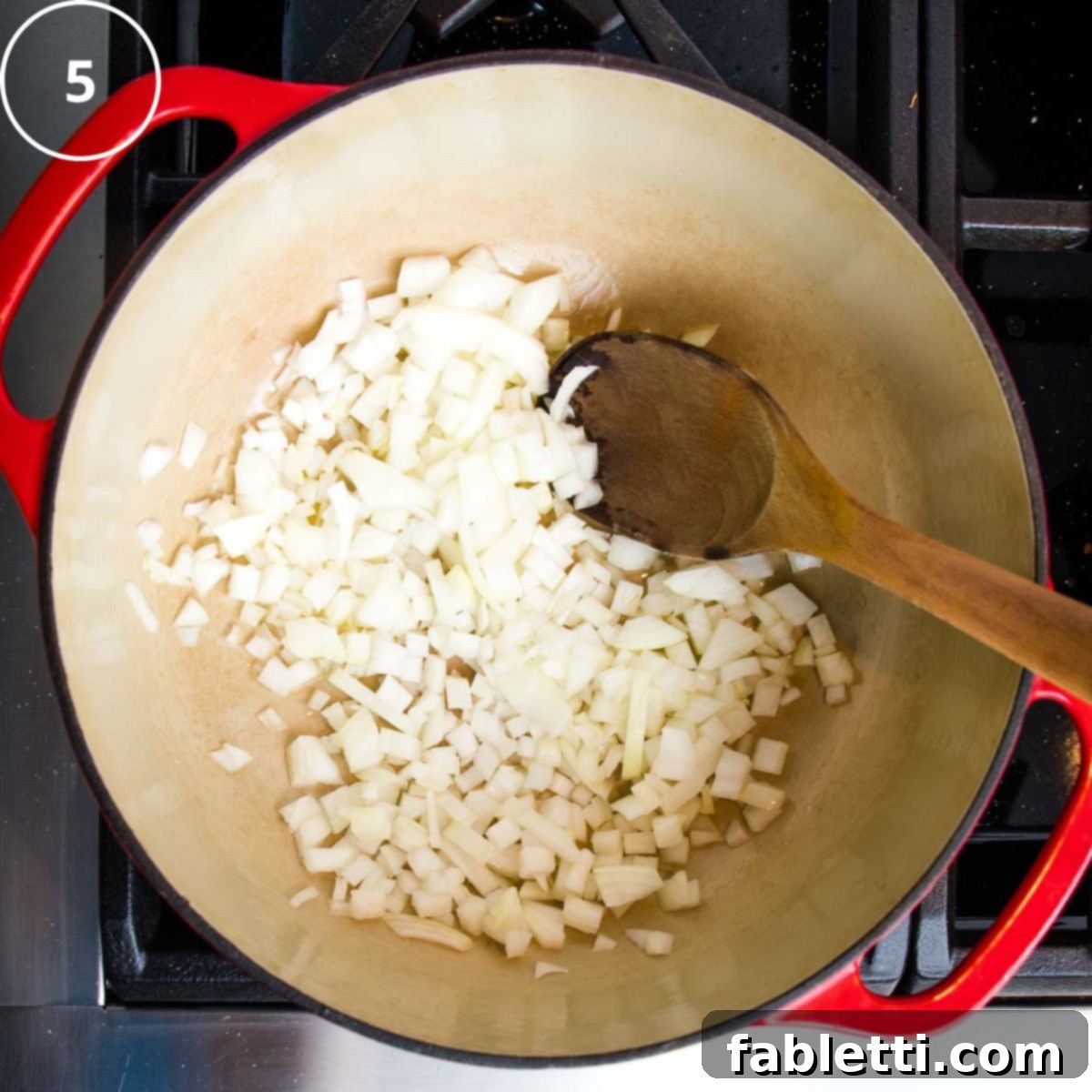 Velvety Vegan Butternut Bliss 14 Diced onions in a dutch oven with a wooden spoon.