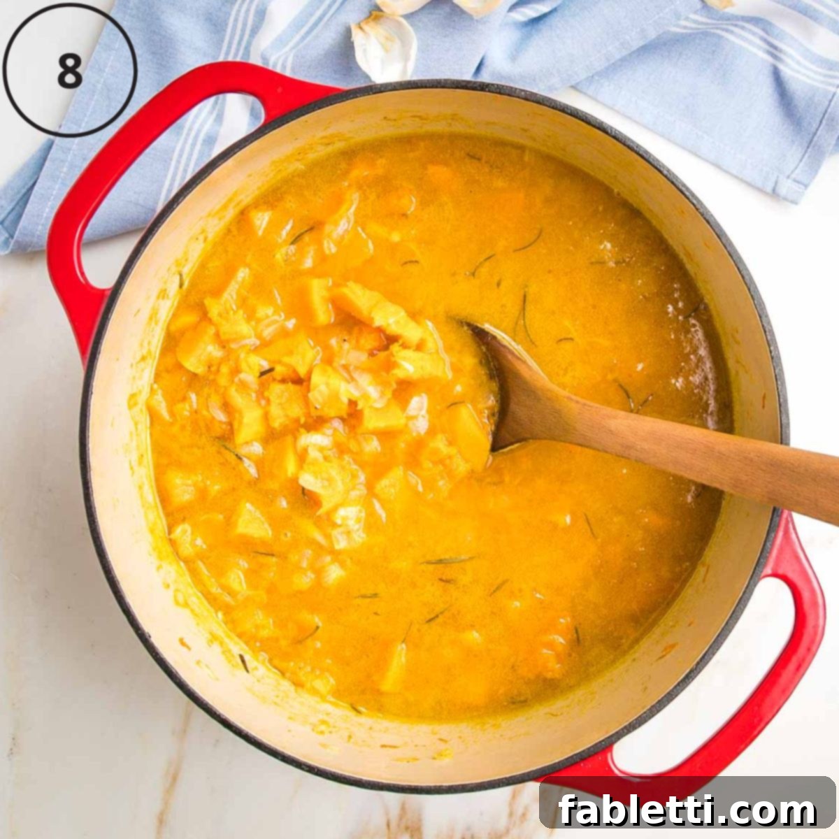 Velvety Vegan Butternut Bliss 17 Butternut squash soup in a dutch oven, chunks of squash and onions floating in orange broth in a dutch oven.
