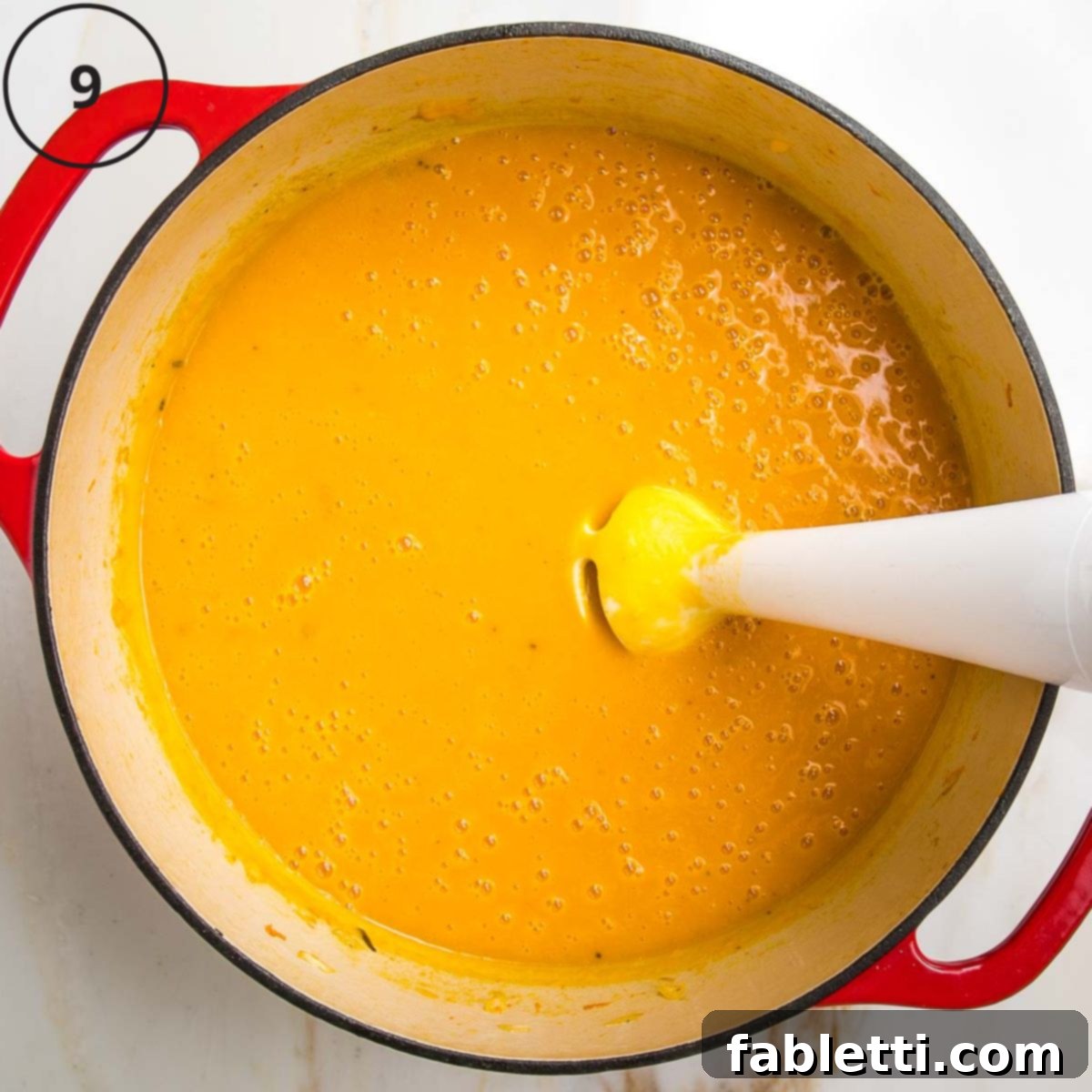Velvety Vegan Butternut Bliss 18 Beautiful orange pureed soup with an immersion blender in a dutch oven.