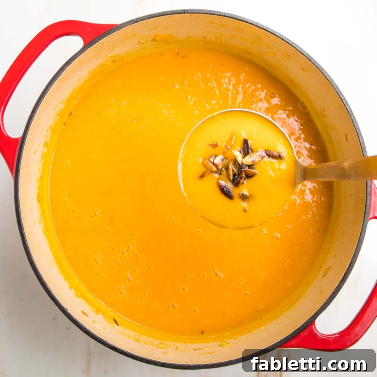 Velvety Vegan Butternut Bliss 19 A ladle of butternut squash soup with toasted pepitas hovering over an entire pot of the creamy orange soup.