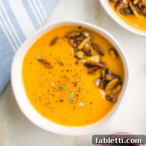 Velvety Vegan Butternut Bliss 21 Bright orange creamy soup in a bowl with toasted pepitas, cracked pepper and fresh herbs.