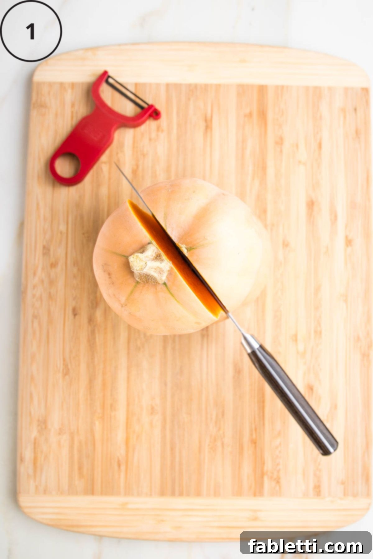 Velvety Vegan Butternut Bliss 6 Butternut squash sitting upright on a cutting board. Knife cutting through the stem and down the center.