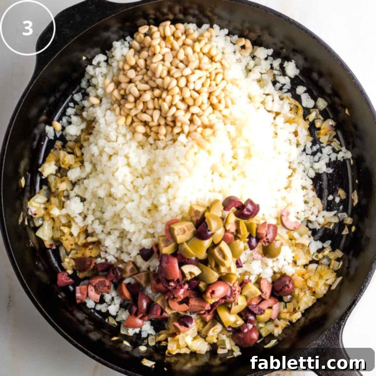 Mediterranean Cauliflower Medley 6 Step 3: Cast iron skillet with riced cauliflower, chopped olives, and pine nuts added over sautéed onions and garlic.
