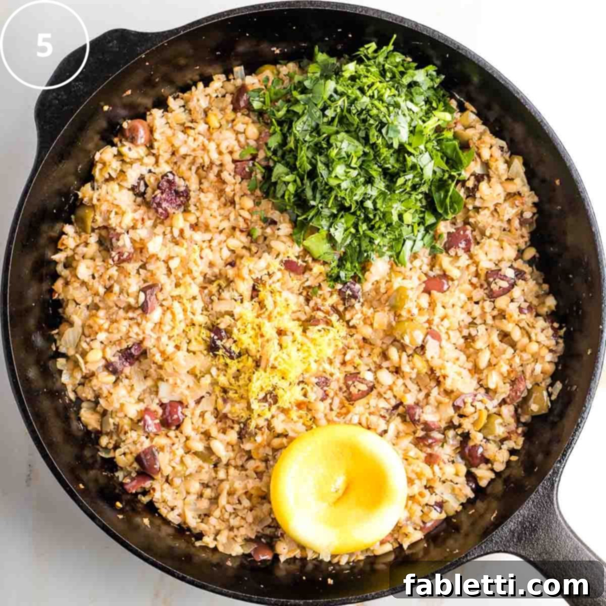 Mediterranean Cauliflower Medley 8 Step 5: Fresh lemon being zested and juiced directly over the cooked cauliflower rice with parsley.