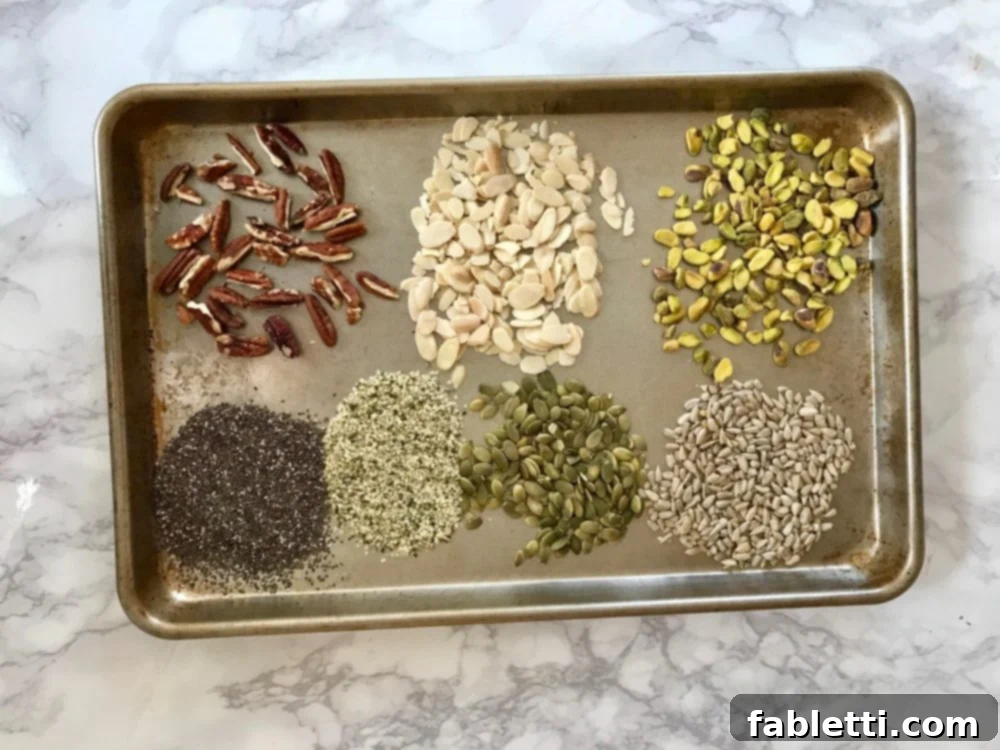 Energy-Packed Chocolate Oat Bars 5 Assortment of raw nuts and seeds laid out on a baking sheet: pecans, almonds, pistachios, pepitas, sunflower seeds, chia seeds, hemp seeds, and dried cherries.