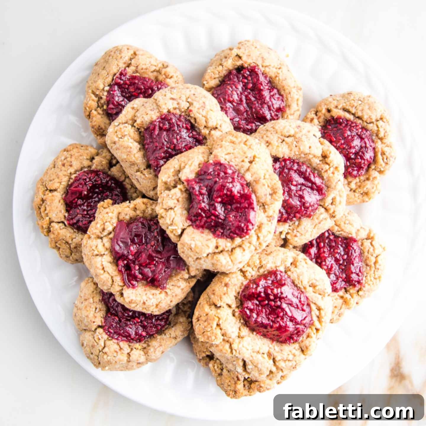 Almond Gem Cookies 2 Close-up of a beautifully baked vegan almond thumbprint cookie with a vibrant jam center.
