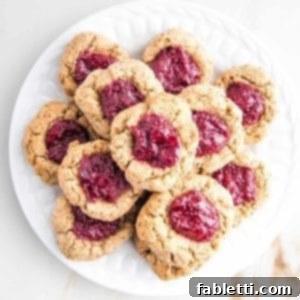 Almond Gem Cookies 12 A white plate piled with healthy thumbprint cookies filled with bright red cranberry chia jam.