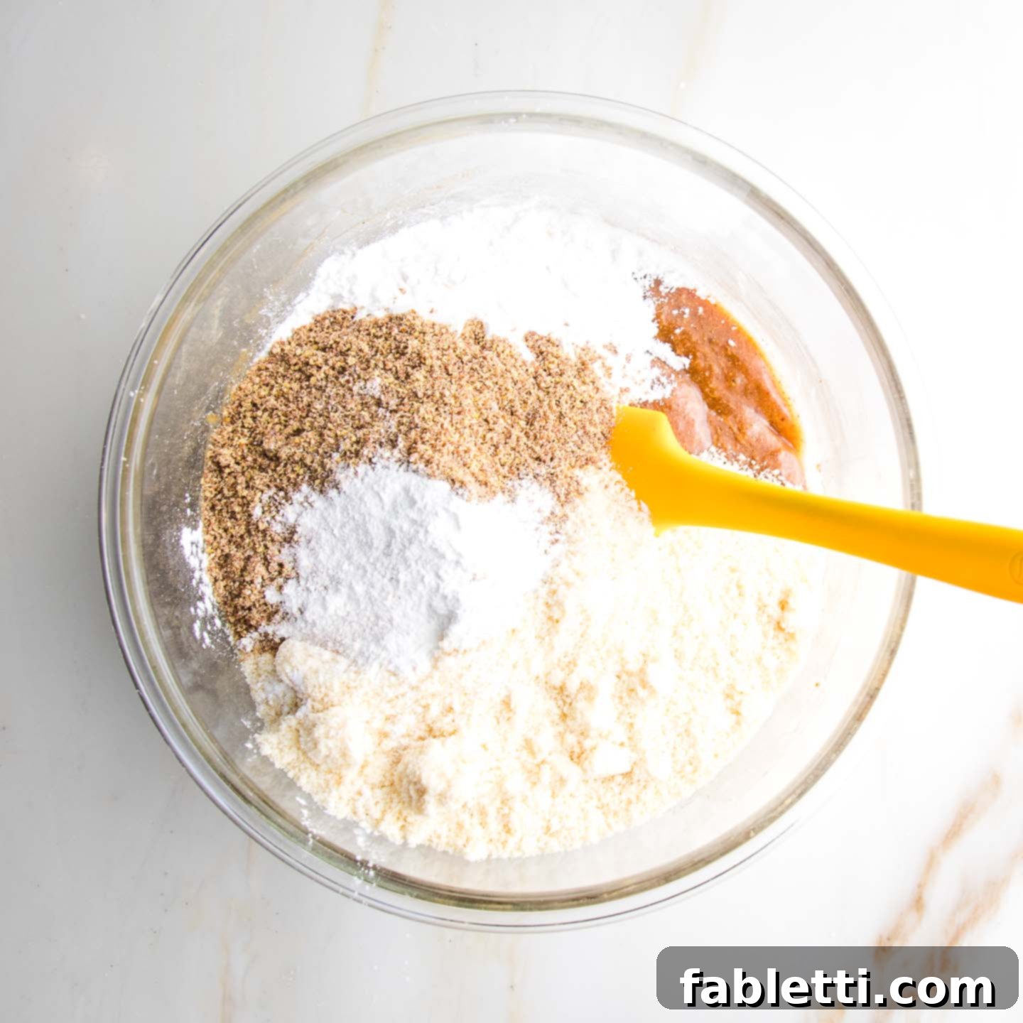 Almond Gem Cookies 6 Dry ingredients like almond flour, ground flax, and arrowroot powder being mixed into the wet ingredients in a glass bowl.