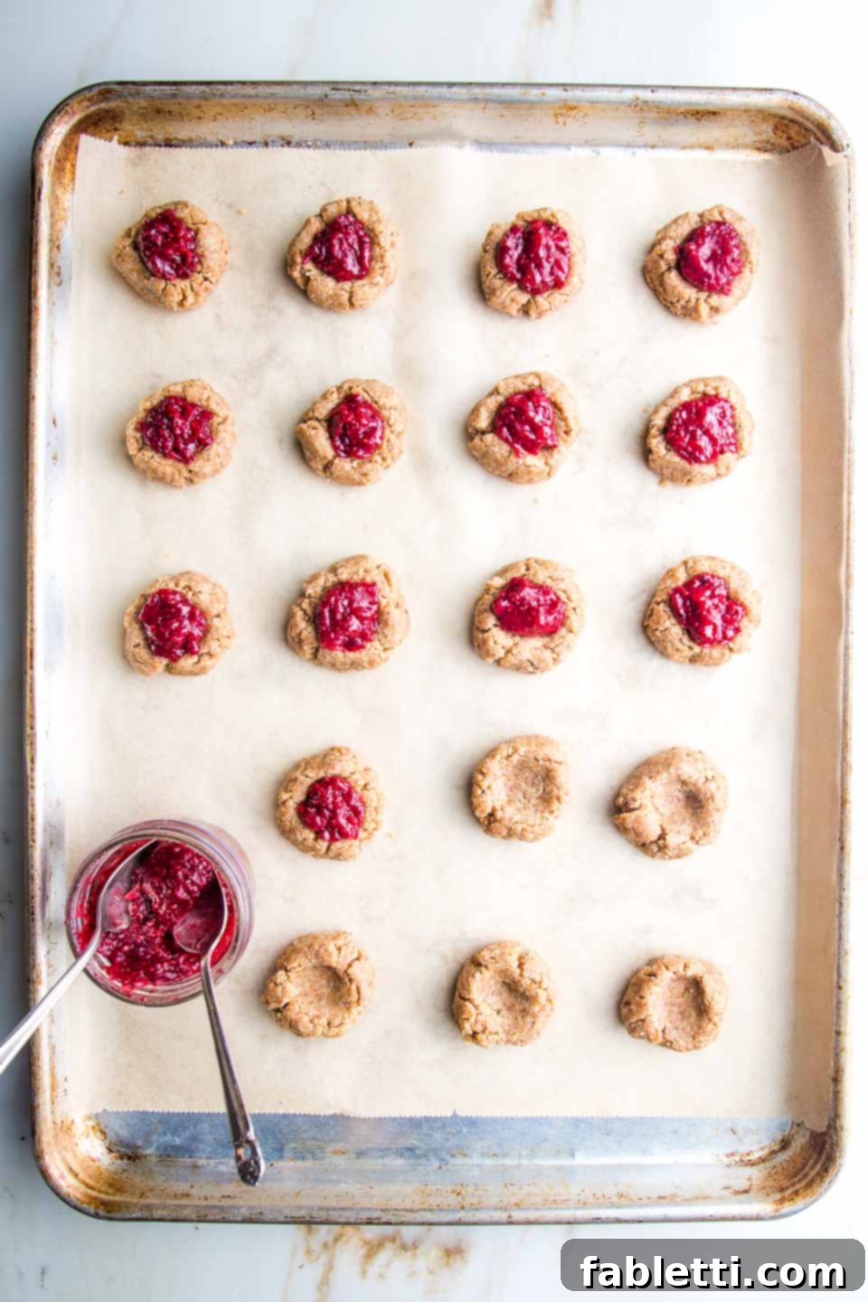Almond Gem Cookies 8 A baking sheet with thumbprint cookies, some filled with bright red cranberry jam, and a small dish of jam ready for filling the rest.