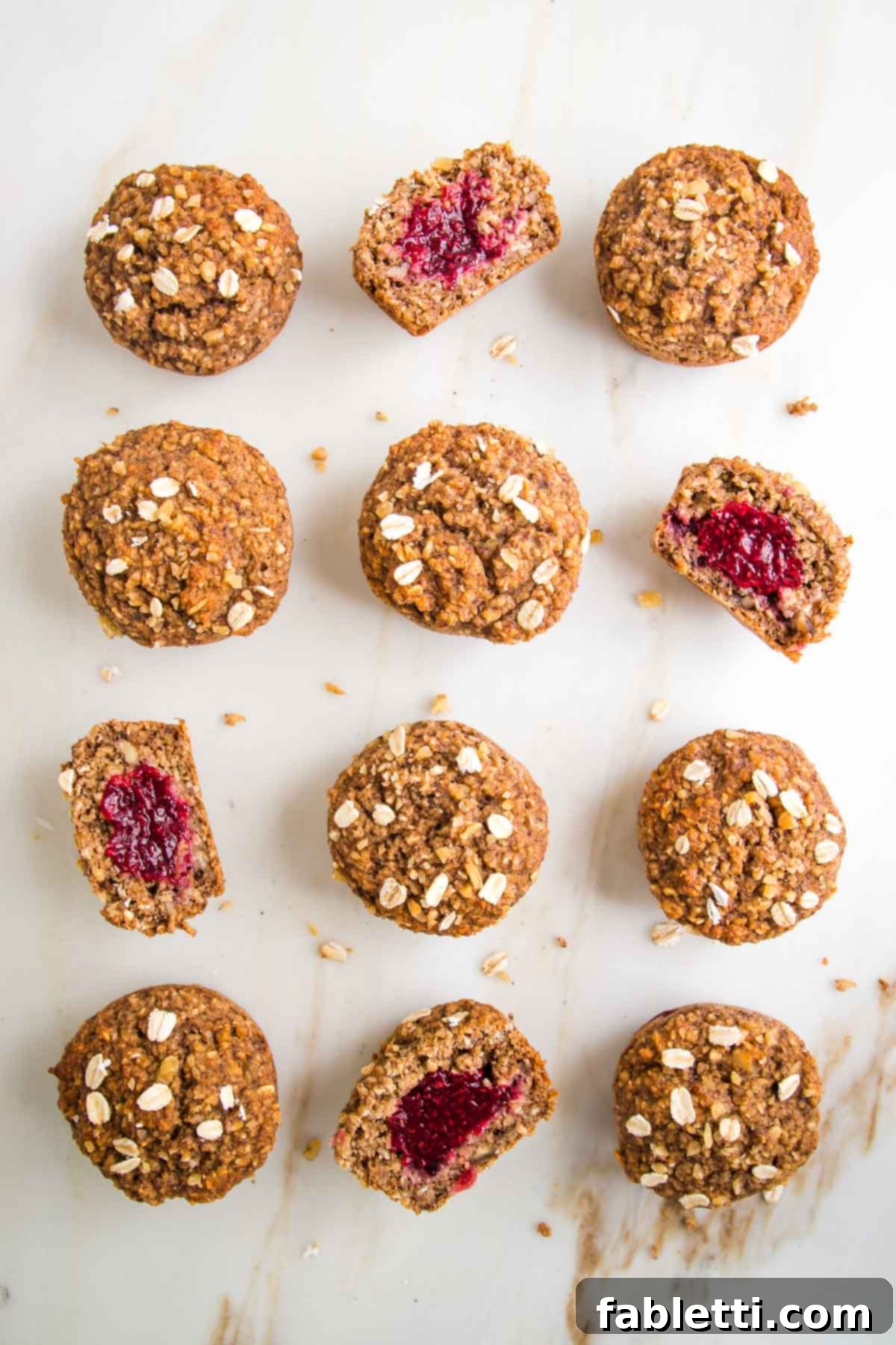 A dozen oatmeal muffins, filled with jam. Several are cut in half so you can see they are filled with jam.